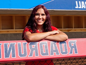 Arianna Valdez leaning on a fence with a Roadrunners sign.